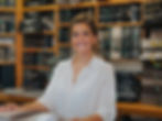 Smiling woman in a white shirt, looking at camera, in a furniture store, with shelves full of fabric swatches in the background