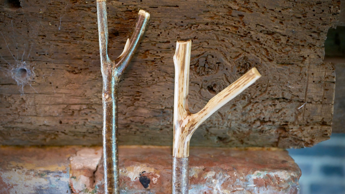 Two forked wooden walking sticks against a rustic wall