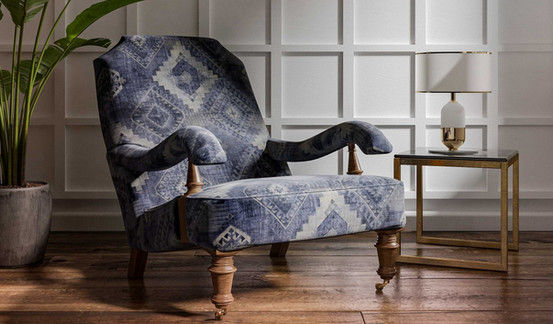 Blue patterned armchair with wooden legs and arms, beside a glass-top end table with a lamp