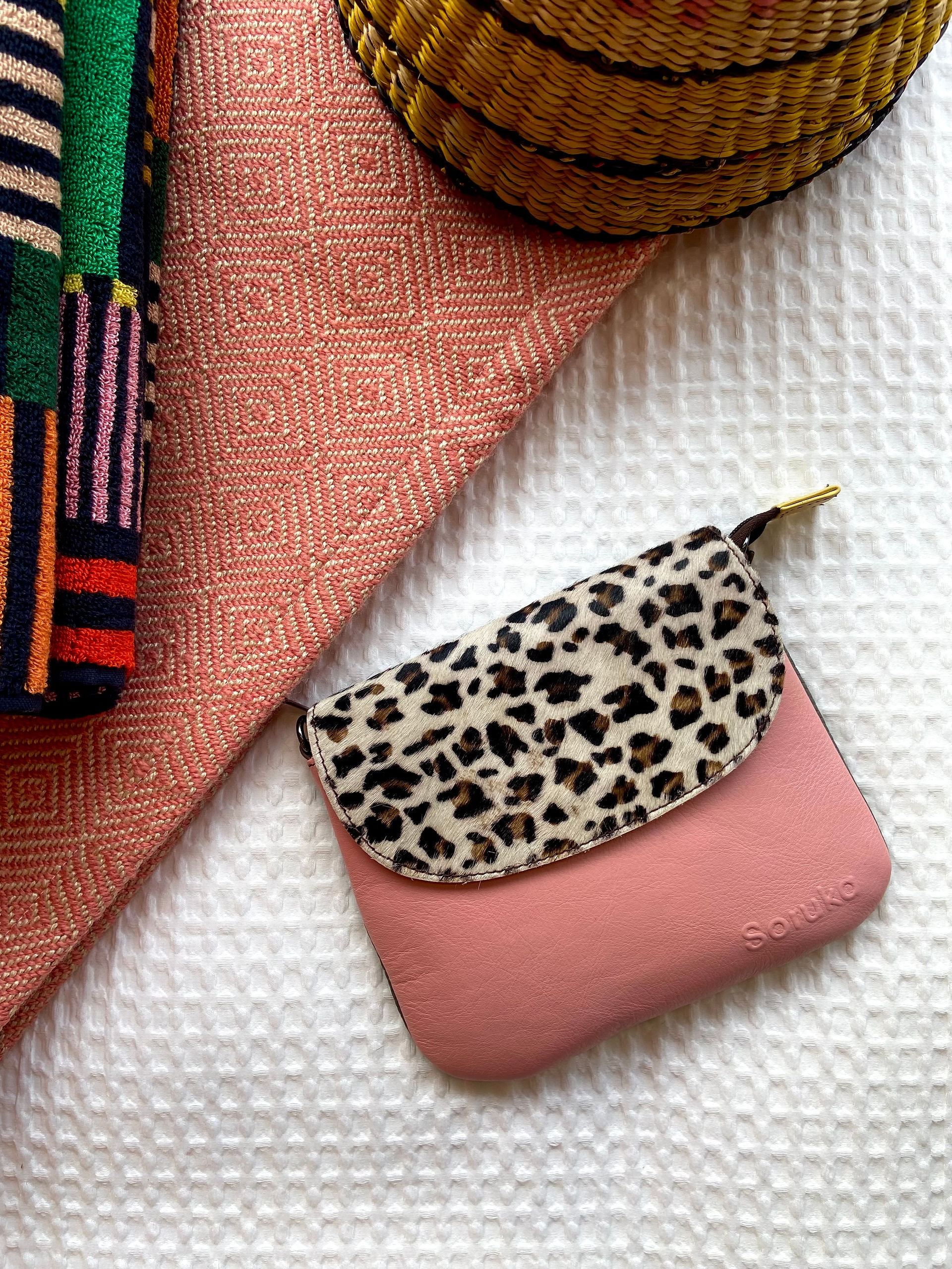 "A triptych of Soruka crossbody bags (pink/leopard, brown/zebra, blue/leopard) on flat-lay display with colourful blankets."