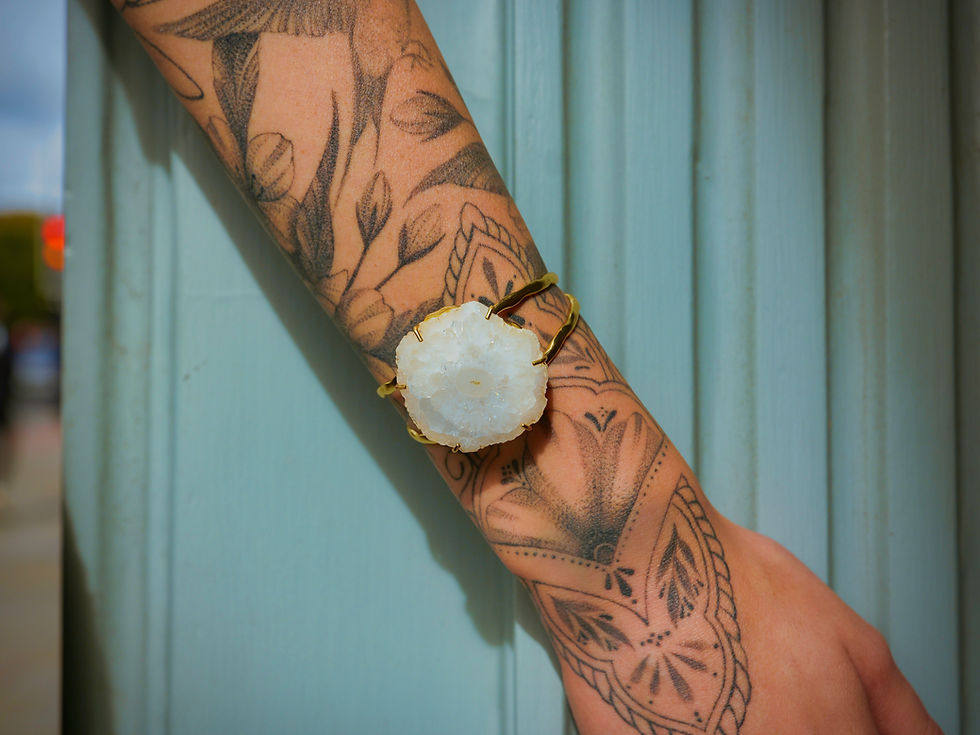 Dveep Solar Quartz Bracelet - Gold cuff bracelet set by Nkuku with a large natural raw white quartz stone worn on a tattooed wrist outside Carvills.