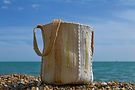 Hand Crafted Artisan Beach Bag sat in front of the blue sea and shingle beach of southern England with a sof blue sky in the background. by Treeless Group..