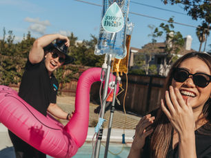 Two IV nurses with a flamingo floatie and an IV bag near the pool