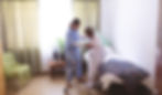 Caregiver assisting a senior to stand up from the bed and use a walker for support.