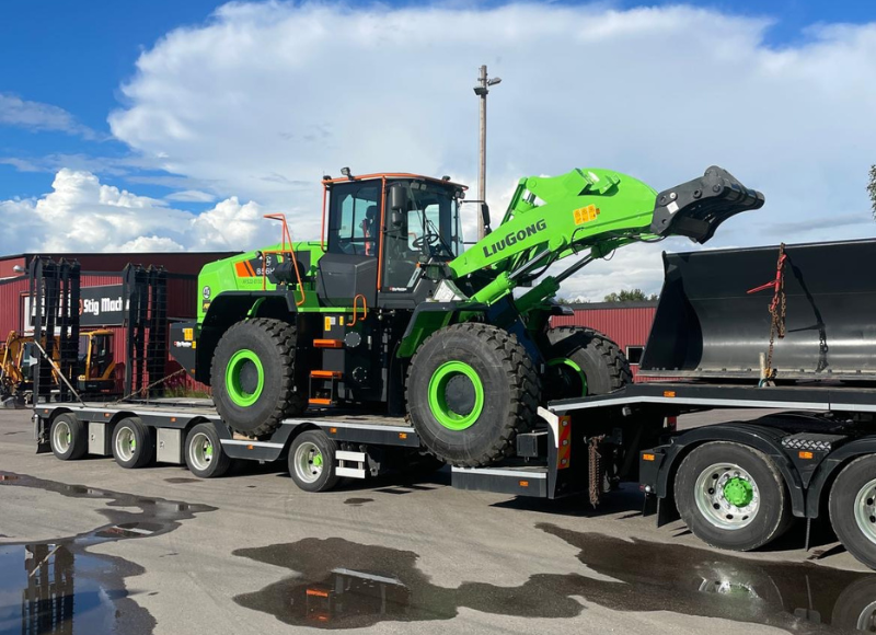 Grön Liugong hjullastare på trailer utanför Stig Machine, redo för leverans eller demo.