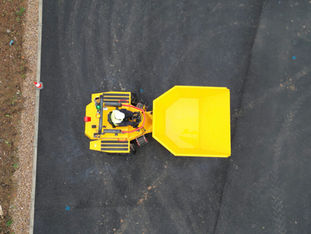 Flygbild ovanifrån på gul Thwaites dumper med förare, stående på asfalterad yta.