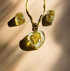 a clear, heart-shaped resin pendant filled with shimmering gold flakes. It hangs from a delicate gold-colored chain