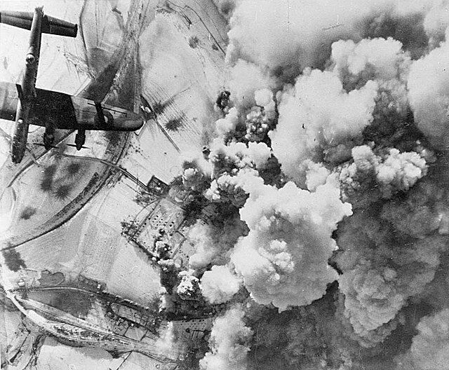 Aerial view of a bomber plane over snowy fields; large plumes of smoke rise from explosions below, creating a dramatic scene.