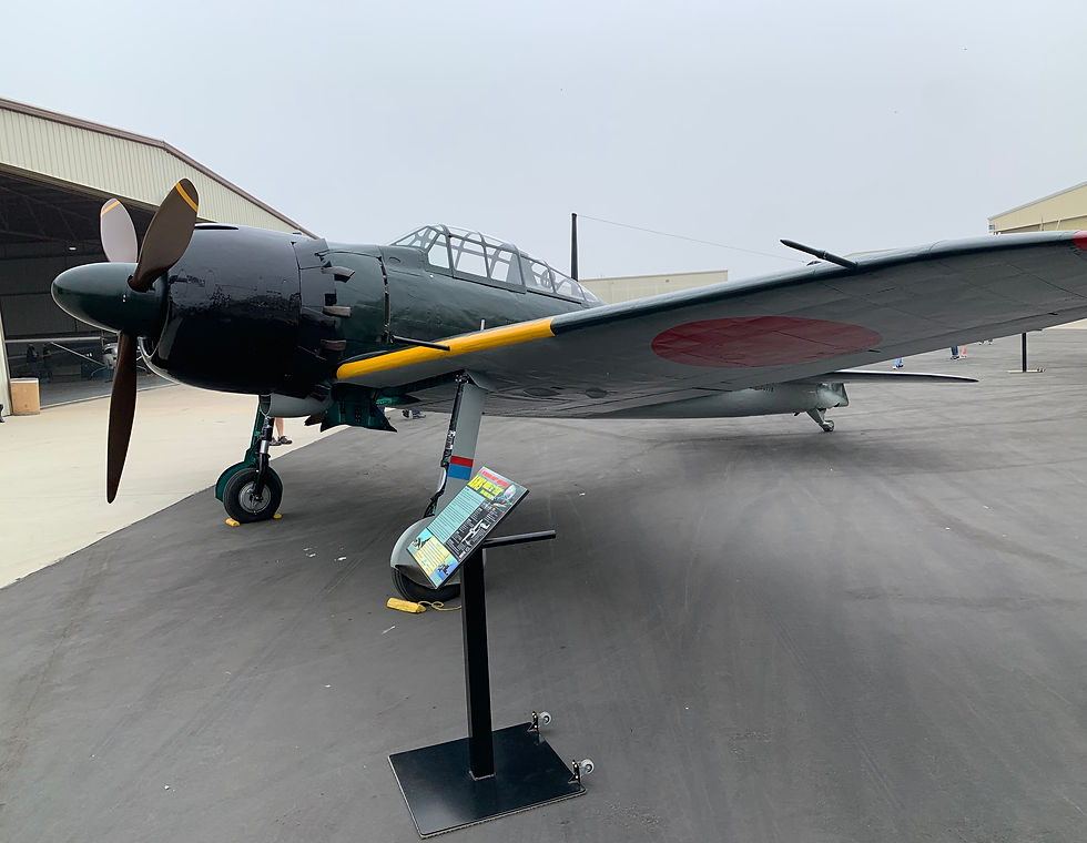 Vintage military aircraft on display outside a hangar. Green fuselage, with red circle on wings. Informative plaque in front. Overcast sky.