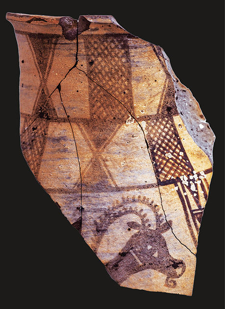 Broken ceramic shard with brown geometric and lattice patterns on a black background, showing cracks and chipped edges