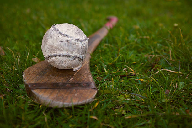 a sliotar and a hurl on a green playing pitch