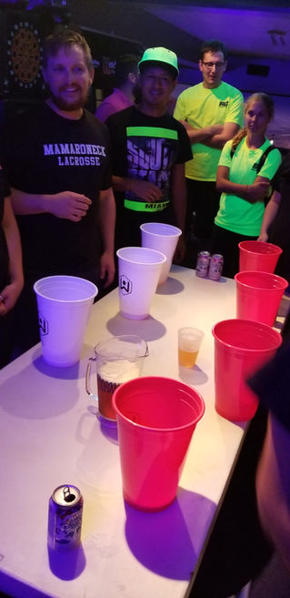 Event guests playing an indoor giant pong party game using oversized plastic cups set up on a long table.