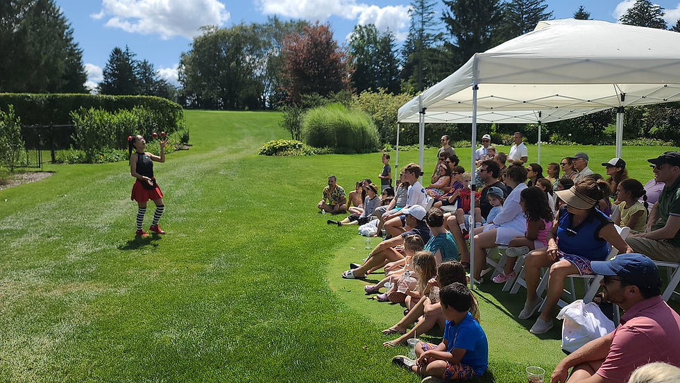 Joyce Kung juggling outdoors for an audience of children and adults seated on a lawn beneath a canopy.