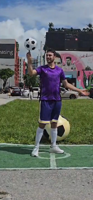 Soccer juggler performer in a purple uniform performing ball tricks at an outdoor event.