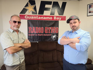 Entertainers posing at AFN Guantanamo Bay radio station with Radio GTMO sign in the background.