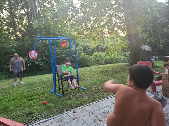 Pitch Splash Game set up outside with a child sitting under a water bucket while another child throws a ball at the target, provided by Magical Memories Entertainment