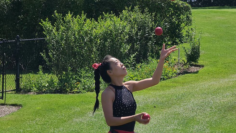 Circus performer juggling red balls outdoors on a grassy lawn.
