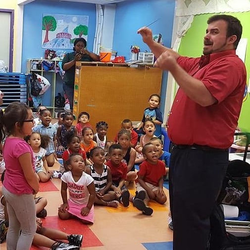 A live magician holding a magic wand and entertaining a group of seated young kids in a classroom setting during a Preschool Party.