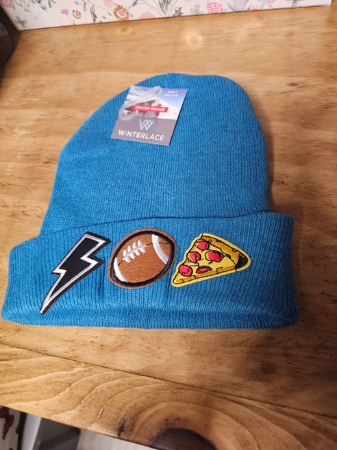 A blue knit beanie decorated with embroidered pizza, football, and lightning bolt patches at a custom Family Day patch bar station