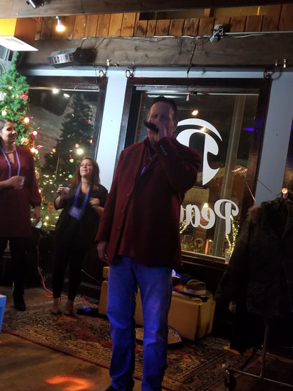 A karaoke night at a holiday event, with guests taking turns singing festive songs on stage, surrounded by cheerful decorations and a lively audience enjoying the performances
