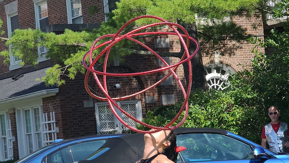 Joyce Kung riding a unicycle while spinning a red hula hoop during an outdoor poolside performance.
