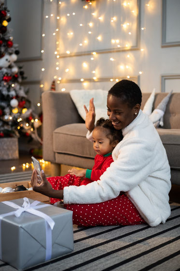 Smiling woman and young child in holiday pajamas waving at a phone screen during a virtual holiday-themed murder mystery event.