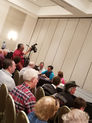 Naathan Phan presenting a magic lecture to a seated audience with a camera operator recording.