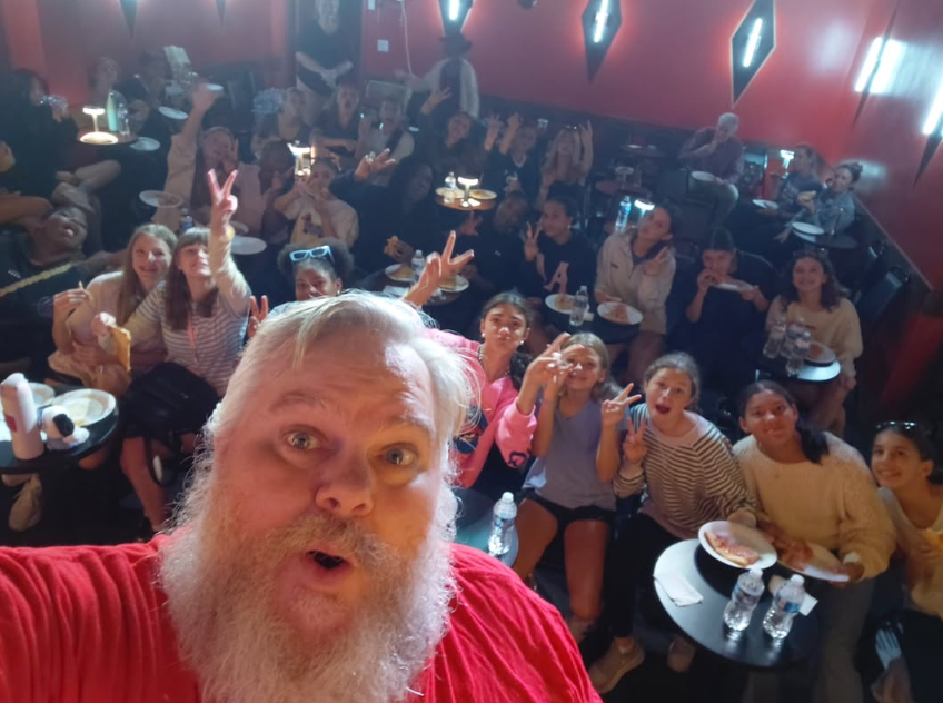 Walt Frasier taking a group selfie with smiling audience members inside an entertainment venue.