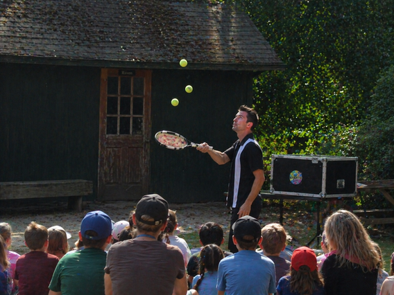Tennis trick performer bouncing multiple tennis balls off one racket during an outdoor show.
