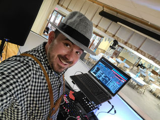 Smiling professional DJ in a hat performing at a private event with laptop and audio setup.