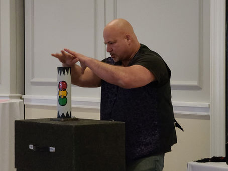 Magician Rob Dell’Aquila, known as the Great Roberto, performing a magic trick with colorful props at an indoor event.