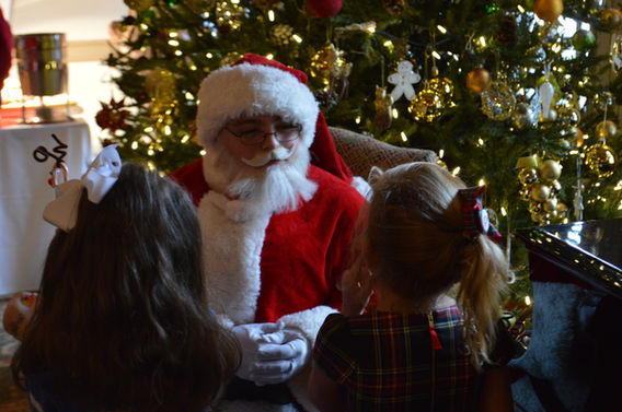 Santa Claus visiting a holiday event, greeting children with a warm smile, posing for photos, and spreading festive cheer in a joyful atmosphere