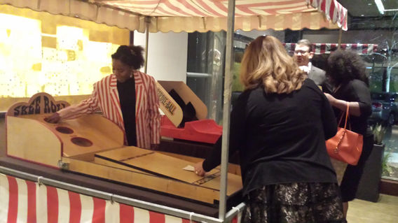 Adults playing Skee Ball and Strike Zone carnival games operated by Magical Memories Entertainment at an indoor event.