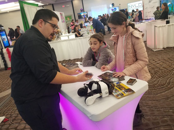 A magician entertains children at a trade show booth, performing magic tricks and captivating young attendees with their engaging performance.