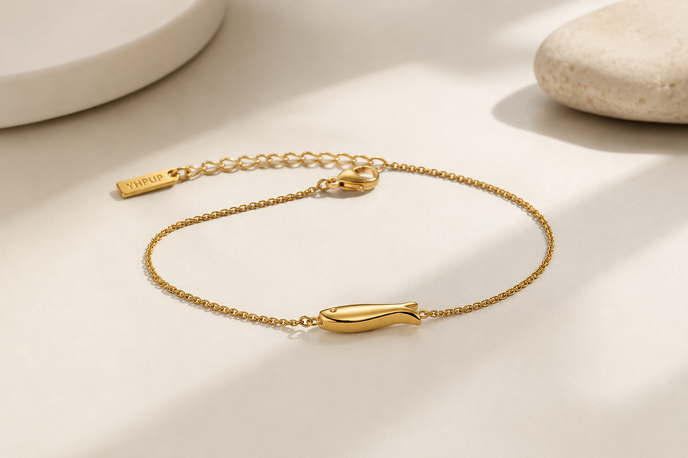 Gold fish chain bracelet from Orizo displayed on a beige surface, featuring a delicate gold chain and a polished fish‑shaped 