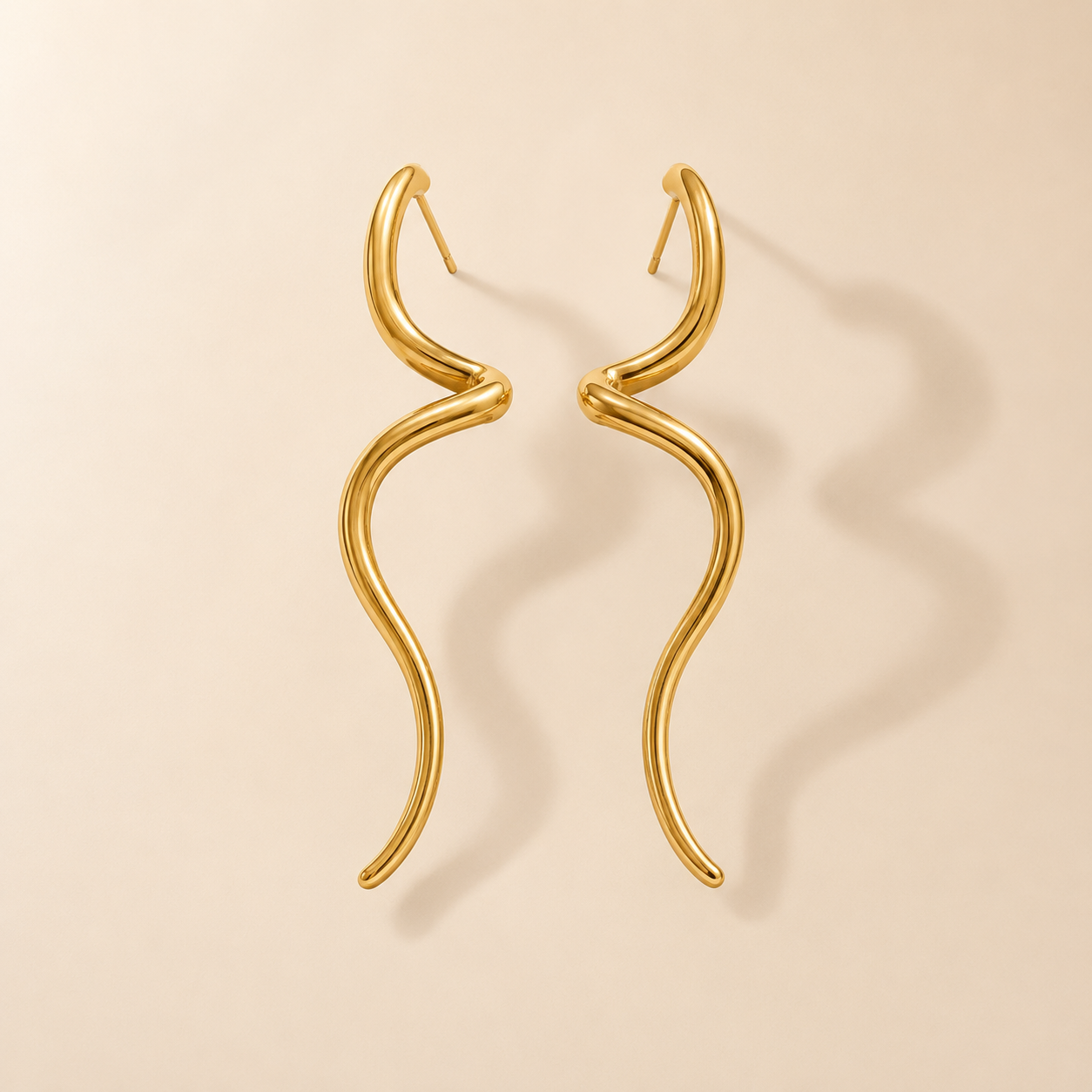 Gold fluid sculptural long drop earrings from Orizo displayed on a beige background, featuring an elegant wavy design and pol