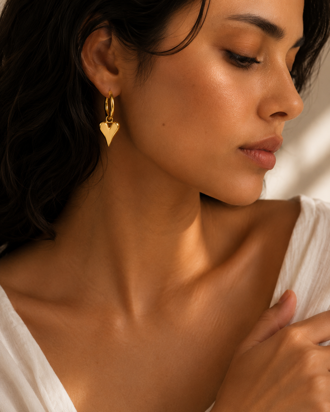 Gold heart huggie hoop earrings from Orizo worn by a woman with a white top, highlighting their polished finish and romantic