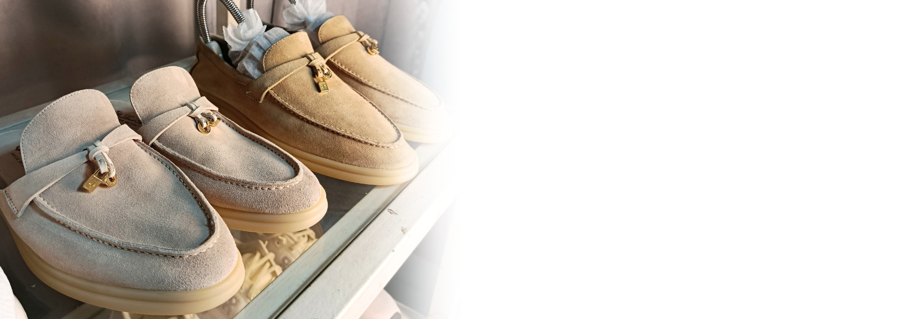 Premium Loro Piana suede loafers and mules with signature gold charms resting with shoe trees on a glass studio shelf, demonstrating expert material-specific care at Sole Revival Bangkok.