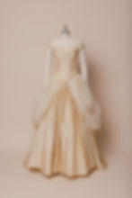 Gold silk off-shoulder wedding dress with corset bodice and draped skirt on dress form against ivory backdrop