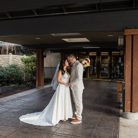 A bride in a wedding dress and groom in tan suit embrace at the entrance of Royal Oaks Country Club in Vancouver, WA on their wedding day