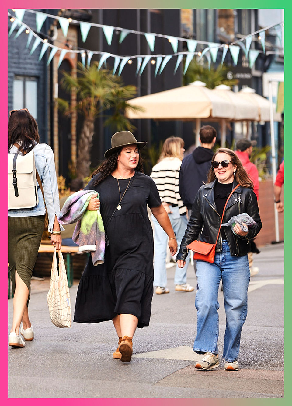 Two women walking and chatting at the Lonsdale Road Street Party, enjoying the lively atmosphere with bunting overhead and people gathered along the street