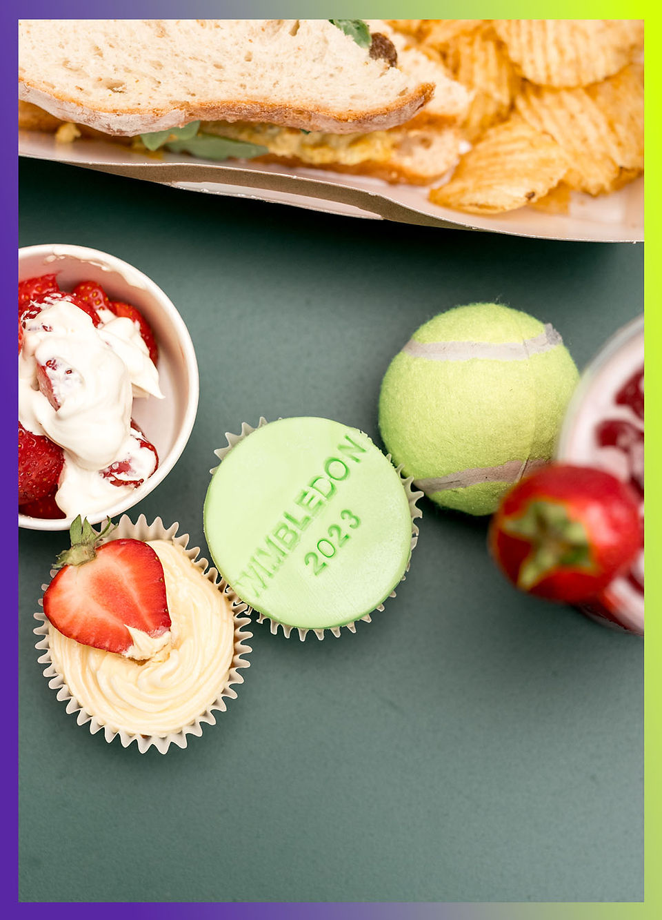 Close-up of Wimbledon-themed cupcakes, strawberries, and a tennis ball on a table.