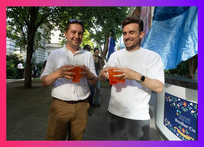 Two smiling men holding four cocktails each, served by BoxBar Co at the Midsummer Fayre.
