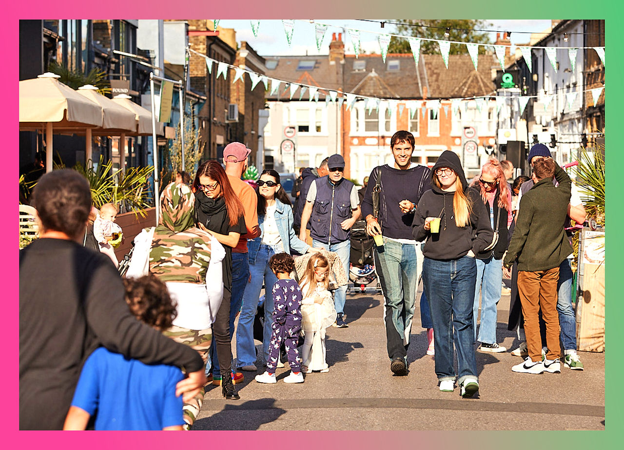 Families and friends strolling down Lonsdale Road, enjoying the festivities of the street party with colorful bunting and vibrant street activities.
