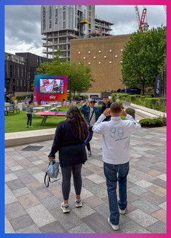 A group of people enjoy a lively outdoor scene at Television Centre, with a large screen showing sports and colourful deck chairs nearby.