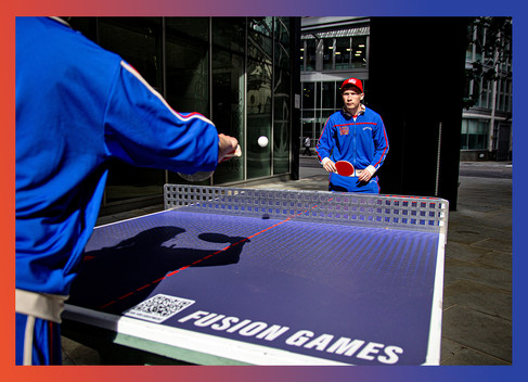 Two players engage in a ping pong match at Fleet Street Quarter. One is in focus, poised to hit the ball, while the other is ready to return. The table is branded with "Fusion Games," adding to the event's lively atmosphere.