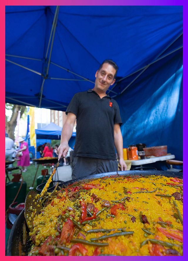 Chef serving giant pan of vibrant paella at the outdoor summer street food stall during the event.
