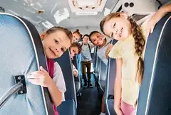 Niños sonriendo y mirando desde los asientos del autobús escolar, apcologistic.com