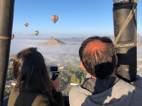 Dos personas en globo mirando el paisaje con más globos y niebla. Vuelos en globo.