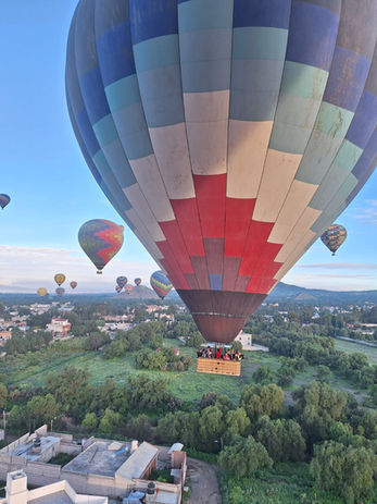 Globos aerostáticos multicolores sobrevolando paisaje verde; Vuelos en globo.